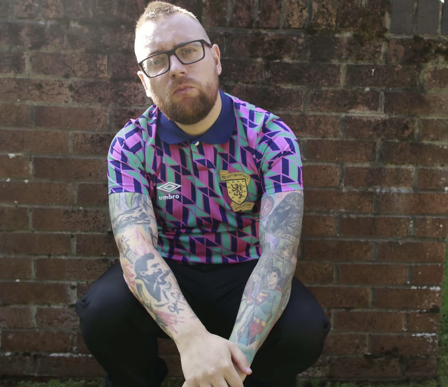 Joe Quinn crouched against a brick wall in a retro Scotland shirt